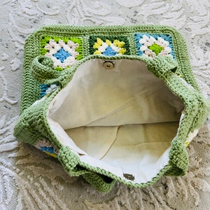 K&ouml;nnte beinhalten: Gr&uuml;ne geh&auml;kelte Tragetasche mit Blumenmuster. Die Tasche ist offen und das Innere ist mit einem wei&szlig;en Stoff ausgekleidet.