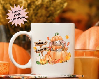 May include: White ceramic mug with a cute cartoon mouse wearing a scarf and sitting inside a pumpkin. The mug has a brown sign that says "Autumn Blessings".