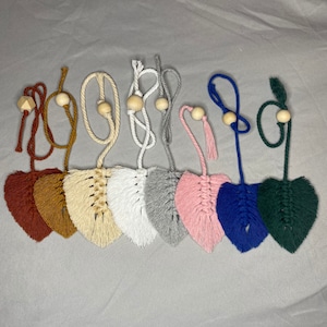 May include: Eight handmade macrame leaf-shaped ornaments with wooden beads and tassels in various colors, including brown, beige, white, gray, pink, blue, and green.