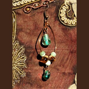 May include: A copper-colored, teardrop-shaped earring with a hook. The earring features a turquoise-colored, teardrop-shaped bead at the top and a cluster of green and amber-colored beads in the middle. A green bead hangs at the bottom.