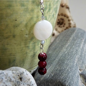 May include: Silver dangle earrings with a white round bead and three red round beads.