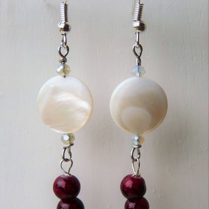 May include: A pair of silver earrings with white shell-like round beads and three burgundy beads hanging from each.