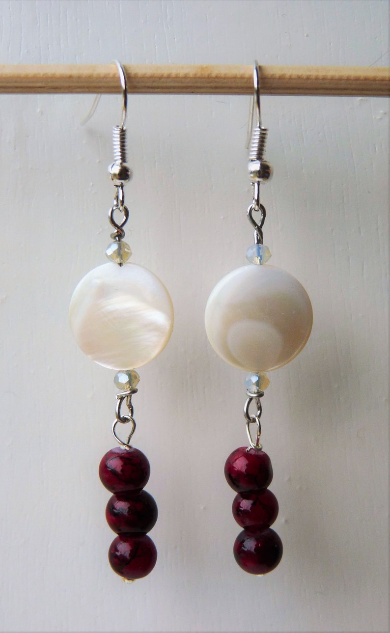 May include: A pair of silver earrings with white shell-like round beads and three burgundy beads hanging from each.