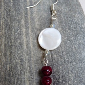 May include: A silver dangle earring with a white round shell bead and three dark red round beads.