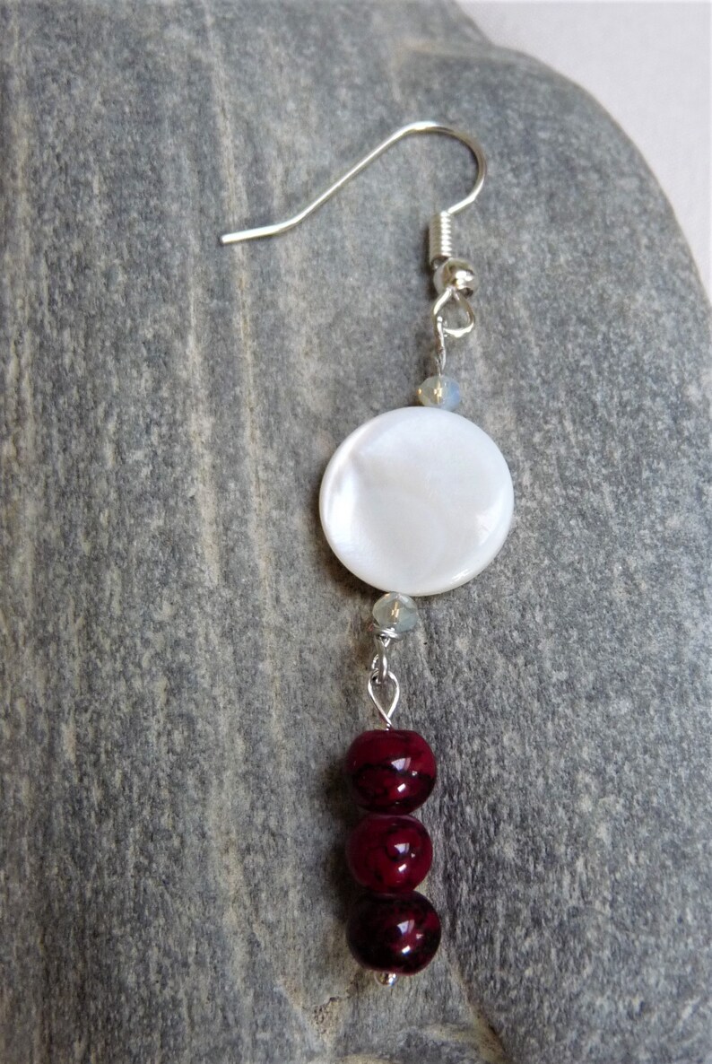 May include: A silver dangle earring with a white round shell bead and three dark red round beads.