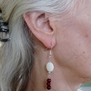 May include: Silver dangle earrings with a white oval bead and red round beads.