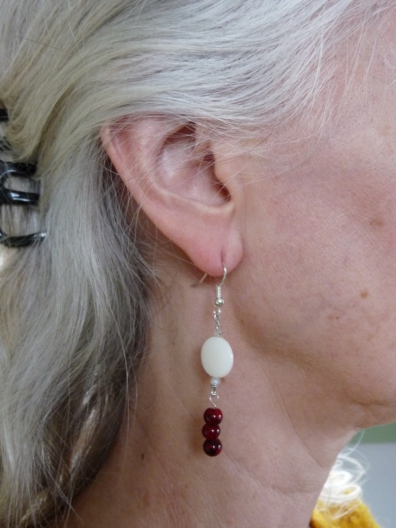 May include: Silver dangle earrings with a white oval bead and red round beads.