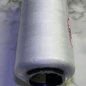 May include: A white spool of thread wrapped in clear plastic. The spool is labeled "WHITE" and has a black and white label with a logo.