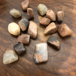 May include: A collection of 15 sunstone tumbled stones in various shades of brown, beige, and white. The stones are smooth and polished, with a natural, earthy look.