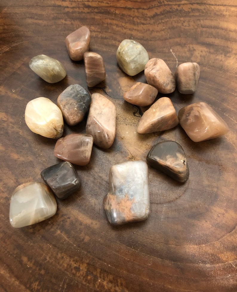 May include: A collection of 15 sunstone tumbled stones in various shades of brown, beige, and white. The stones are smooth and polished, with a natural, earthy look.