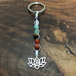 May include: A keychain with a silver lotus flower charm and Om symbol, strung with gemstone beads in purple, green, brown, and red. The keychain is attached to a silver ring. The beads are in various sizes.