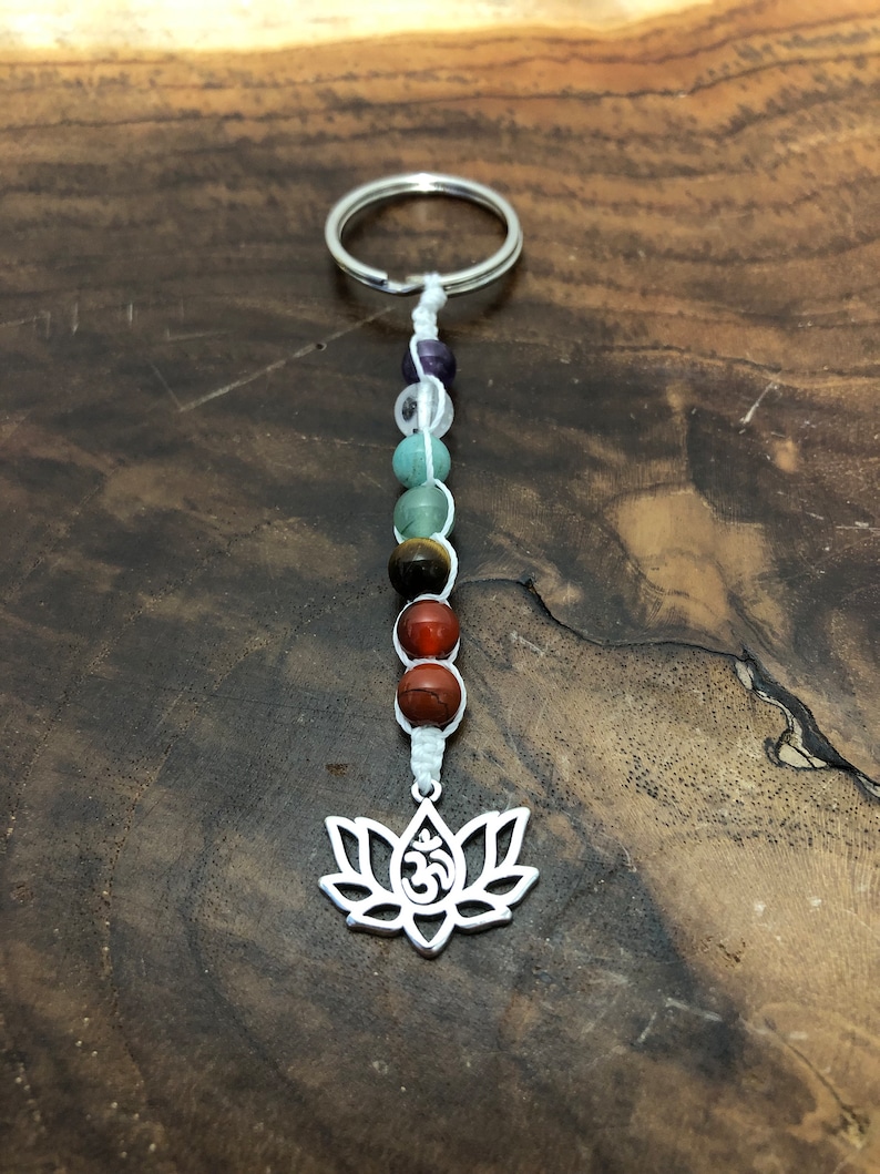 May include: A keychain with a silver lotus flower charm and Om symbol, strung with gemstone beads in purple, green, brown, and red. The keychain is attached to a silver ring. The beads are in various sizes.