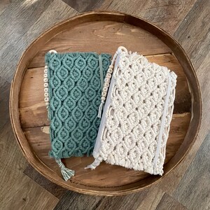 May include: Two macrame wall hangings with wooden bead tassels. The wall hangings are in a light green and white color. The tassels spell out the names "Natalie" and "Maggie".
