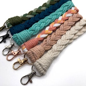 May include: Five braided keychains in various colors, including green, blue, pink, and white. Each keychain has a silver or gold metal key ring.