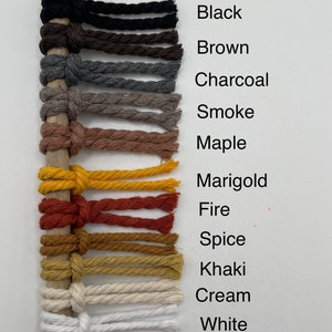 Puede incluir: Primer plano de 12 cuerdas de algod&oacute;n de diferentes colores con un palo de madera detr&aacute;s. Los colores son negro, marr&oacute;n, carb&oacute;n, humo, arce, cal&eacute;ndula, fuego, especias, caqui, crema y blanco.