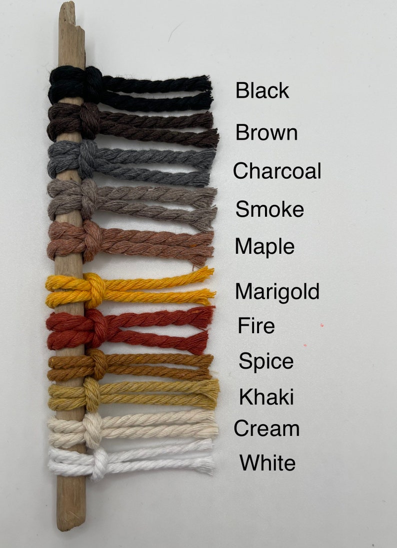 Puede incluir: Primer plano de 12 cuerdas de algod&oacute;n de diferentes colores con un palo de madera detr&aacute;s. Los colores son negro, marr&oacute;n, carb&oacute;n, humo, arce, cal&eacute;ndula, fuego, especias, caqui, crema y blanco.