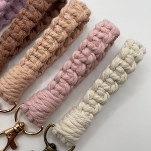 May include: Four crocheted keychains in shades of brown, beige, pink, and white with gold and bronze key rings.