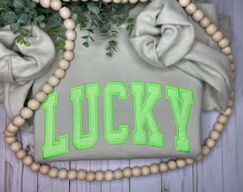 May include: A light gray sweatshirt with the word "LUCKY" in green glitter letters.
