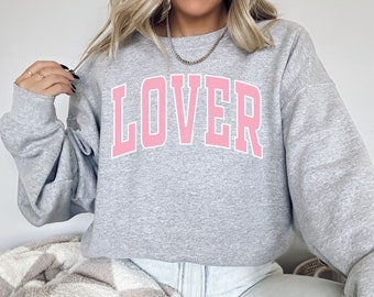 May include: A gray sweatshirt with the word "LOVER" printed in pink letters. The sweatshirt has a relaxed fit and a crew neck.