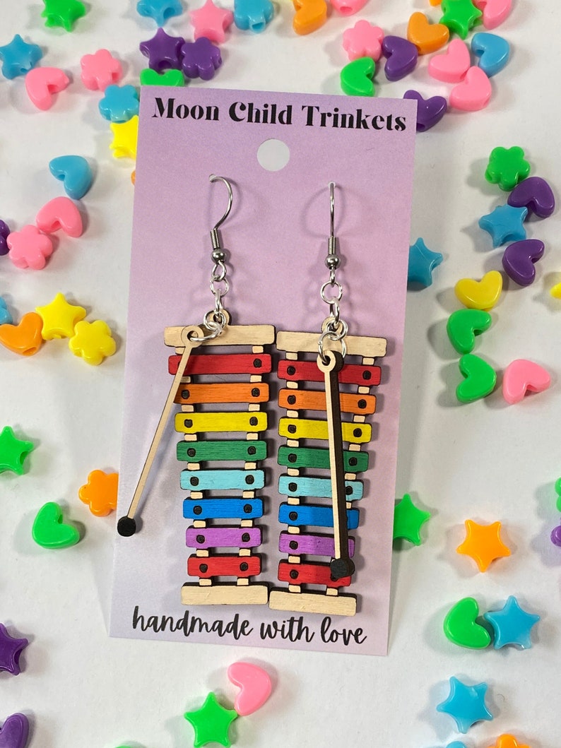 Puede incluir: Pendientes de xil&oacute;fono arco&iacute;ris con ganchos plateados. El xil&oacute;fono est&aacute; hecho de madera y tiene un mazo negro. Los pendientes est&aacute;n hechos a mano con amor. Moon Child Trinkets.