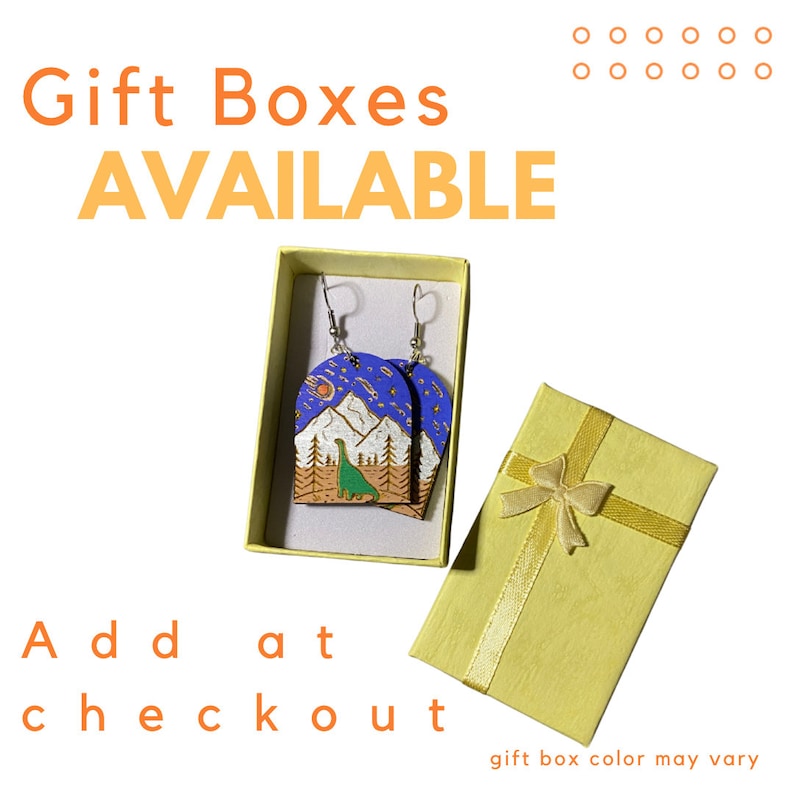 Puede incluir: Un par de pendientes de madera azul y marr&oacute;n con una escena de monta&ntilde;a y un dinosaurio. Los pendientes est&aacute;n en una caja de regalo amarilla con una cinta dorada. Las cajas de regalo est&aacute;n disponibles en la caja. El color de la caja de regalo puede variar.