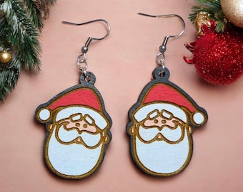 May include: A pair of wooden earrings featuring a cartoon Santa Claus face with a red hat, white beard, and brown eyes. The earrings are attached to silver hooks.