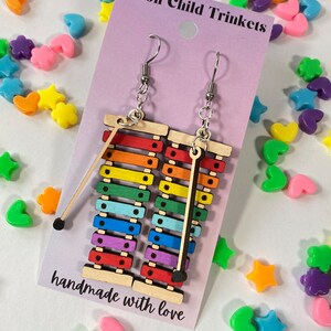 Puede incluir: Pendientes de xil&oacute;fono arco&iacute;ris con ganchos plateados. Los pendientes est&aacute;n hechos de madera y tienen un mazo negro unido a cada uno. Los pendientes est&aacute;n hechos a mano y la tarjeta dice "Moon Child Trinkets" y "hecho con amor".