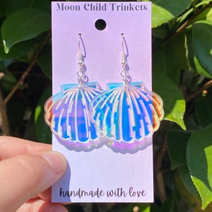 May include: A pair of iridescent seashell earrings on a purple card with the text "Moon Child Trinkets" and "handmade with love".