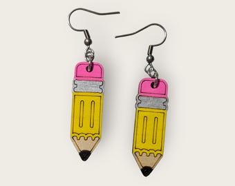 May include: A pair of earrings shaped like yellow pencils with pink erasers and silver bands. The earrings have silver hooks.