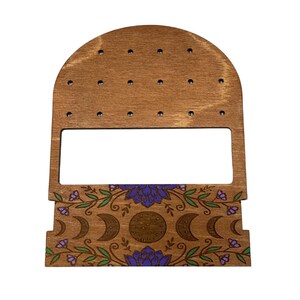 May include: Wooden earring display stand with a crescent moon and floral design. The stand has a top section with holes for earrings and a bottom section with a decorative design.
