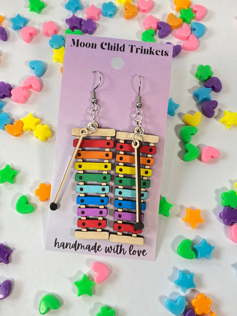 Puede incluir: Pendientes de xil&oacute;fono arco&iacute;ris con ganchos plateados. Los pendientes est&aacute;n hechos de madera y tienen un mazo negro unido a cada uno. La tarjeta dice "Moon Child Trinkets" y "hecho a mano con amor".
