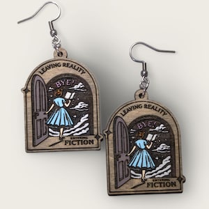 May include: A pair of wooden earrings with a whimsical design. Each earring features a woman walking through a doorway with the text "Leaving Reality Bye! Entering Fiction".