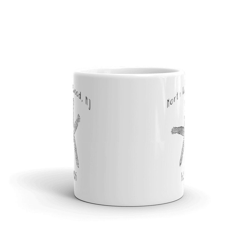 May include: White ceramic mug with a black and white illustration of a starfish on each side. The text "North Wildwood, NJ" appears on the left side of the mug and "North Wildwood, NJ" appears on the right side of the mug.