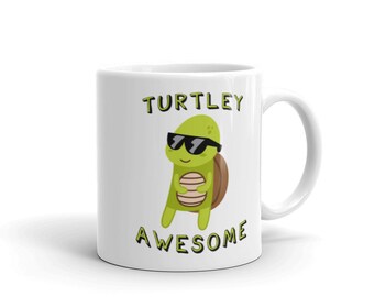 Może przedstawiać: Biały kubek ceramiczny z zielonym rysunkiem żółwia w okularach przeciwsłonecznych i napisem "TURTLEY AWESOME" w kolorze żółtym.
