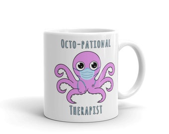 May include: White ceramic coffee mug featuring a pink octopus wearing a blue face mask and a stethoscope. The text "Octo-pational Therapist" is printed on the mug.