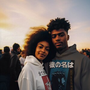 May include: Two people wearing hoodies with graphic designs. The person on the left is wearing a white hoodie with Japanese text and a graphic of a person on a cross. The person on the right is wearing a gray hoodie with Japanese text and a graphic of Jesus on a cross. The text on the hoodie says "His name shall be called".