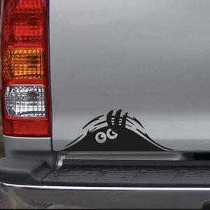 May include: A black and white vinyl sticker of a monster peeking out from behind a car door. The monster has two large eyes and a single claw.