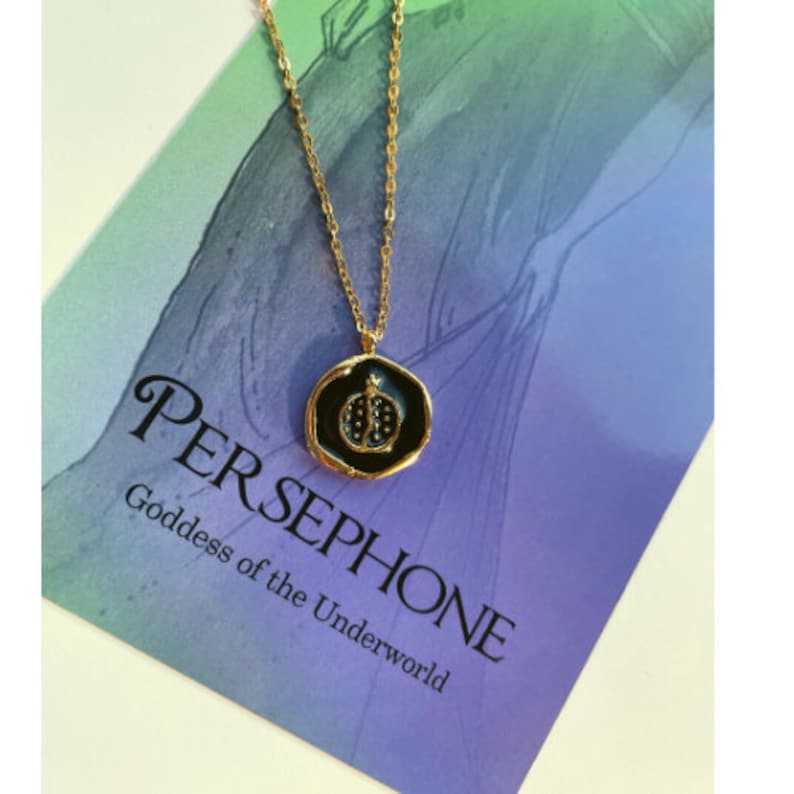 May include: A gold chain necklace with a black enamel pendant featuring a pomegranate design. The pendant has the text "PERSEPHONE Goddess of the Underworld" on the card.