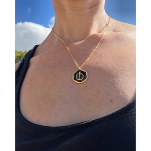 May include: A gold chain necklace with a black and gold pendant featuring a ladybug design. The pendant is octagonal in shape and has a textured surface.