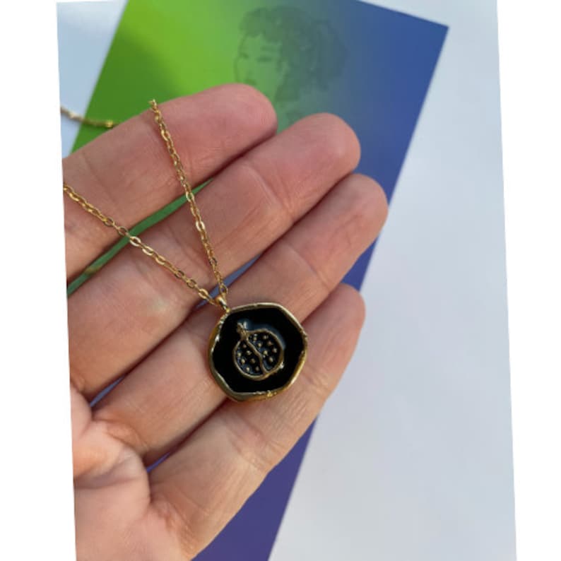 May include: A gold chain necklace with a black enamel pendant featuring a pomegranate design.