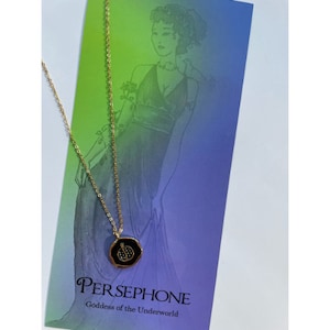 May include: Gold chain necklace with a black enamel pendant featuring a pomegranate design. The pendant has a gold rim and small clear stones. The necklace is displayed on a card with the text "PERSEPHONE Goddess of the Underworld".