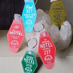 Puede incluir: Cinco llaveros coloridos con forma de llaves de habitaci&oacute;n de motel. Cada llavero tiene un nombre de hotel y un n&uacute;mero de habitaci&oacute;n diferentes. Los llaveros son de pl&aacute;stico y tienen un acabado brillante.