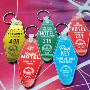 Puede incluir: Un conjunto de seis llaveros con forma de tarjetas de llave de motel vintage. Los llaveros son de varios colores, incluyendo rojo, azul, verde y amarillo. Cada llavero presenta un nombre de hotel y una ubicaci&oacute;n diferentes, como "Stardust Las Vegas, NV", "The Great Northern Hotel Twin Peaks, WA", "Rosebud Motel", "The Overlook Hotel Sidewinder, CO" y "Pool Key".
