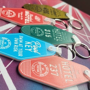 Puede incluir: Cinco llaveros de motel coloridos con diferentes dise&ntilde;os y textos. Los llaveros son rojos, verdes, azules y naranjas. El texto en los llaveros incluye "Pool Key", "Swim at your own risk", "Hotel", "Stardust Motel" y "The Overlook Hotel".