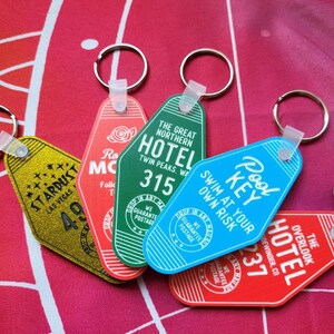 Puede incluir: Cinco llaveros de hotel de estilo vintage con diferentes dise&ntilde;os y colores. Los llaveros presentan los nombres de hoteles, incluyendo "Stardust Las Vegas", "The Great Northern Hotel", "Pool Key", "The Overlook Hotel" y "Ro Mc", con n&uacute;meros de habitaci&oacute;n y otros detalles. Los llaveros est&aacute;n hechos de metal y pl&aacute;stico y tienen una est&eacute;tica retro.