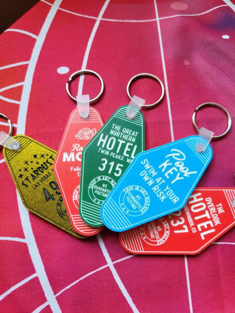 Puede incluir: Cinco llaveros de hotel de estilo vintage con diferentes dise&ntilde;os y colores. Los llaveros presentan los nombres de hoteles, incluyendo "Stardust Las Vegas", "The Great Northern Hotel", "Pool Key", "The Overlook Hotel" y "Ro Mc", con n&uacute;meros de habitaci&oacute;n y otros detalles. Los llaveros est&aacute;n hechos de metal y pl&aacute;stico y tienen una est&eacute;tica retro.