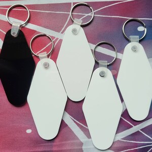 Puede incluir: Cinco llaveros con formas de etiquetas de llave de motel en blanco, blanco y negro. Los llaveros est&aacute;n unidos a llaveros de plata.