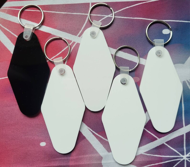 Puede incluir: Cinco llaveros con formas de etiquetas de llave de motel en blanco, blanco y negro. Los llaveros est&aacute;n unidos a llaveros de plata.