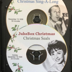 May include: Two vintage Christmas-themed CDs in a black case. The top CD is labeled "JukeBox Christmas Christmas Sing-A-Long" with a photo of a man. The bottom CD is "JukeBox Christmas Christmas Seals" with a photo of Eydie Gorm&eacute;.