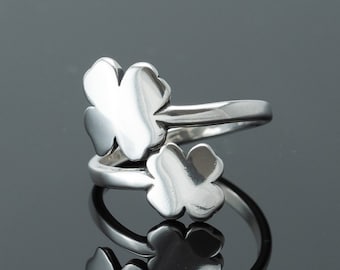 Op de afbeelding: Een zilveren ring met twee klavertjesvier designs. De ring ligt op een grijze achtergrond.